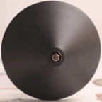 A close-up of a matte black dome-shaped object, likely a lamp shade or decorative dome, with a small metallic circular detail at the center, set against a light beige background.