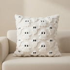 A square white throw pillow with a 3D textured pattern of cute ghost figures, resting on a light beige sofa against a neutral beige wall.