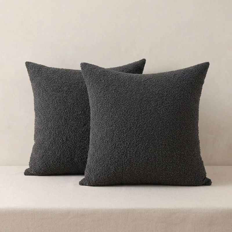 Two dark gray textured pillows on a beige sofa against a neutral wall.