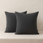 Two dark gray textured pillows on a beige sofa against a neutral wall.