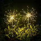 Two solar-powered dandelion-shaped LED light stakes glowing with warm white lights in a dark garden setting.