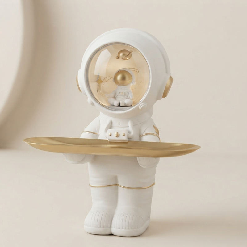 A white astronaut figurine holding a gold-colored tray, set against a soft beige background.