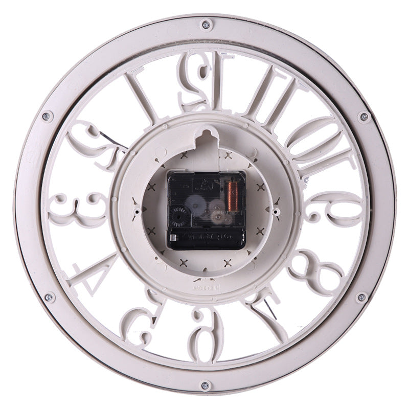 A round wall clock shown from the back, featuring a white outer frame with cutout Roman numerals and a visible black and white mechanical movement mechanism in the center.