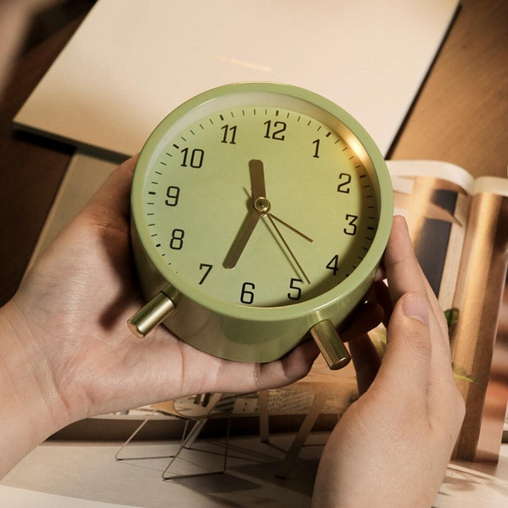 Green alarm clock held by hands with a blurred background