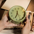 Green alarm clock held by hands with a blurred background