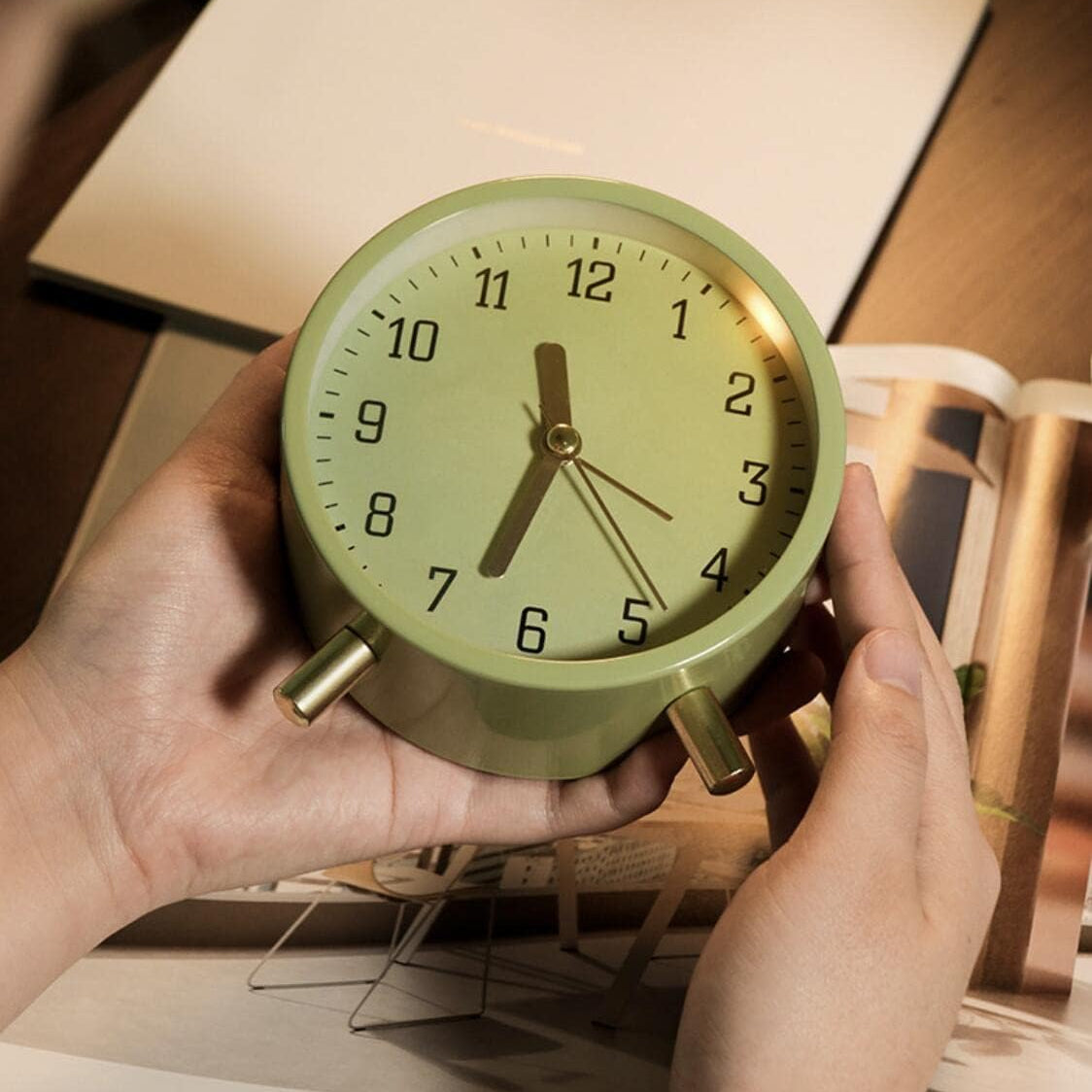 Green alarm clock held by hands with a blurred background