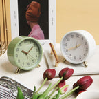 Two alarm clocks, one green and one white, on a surface with tulips and a magazine.