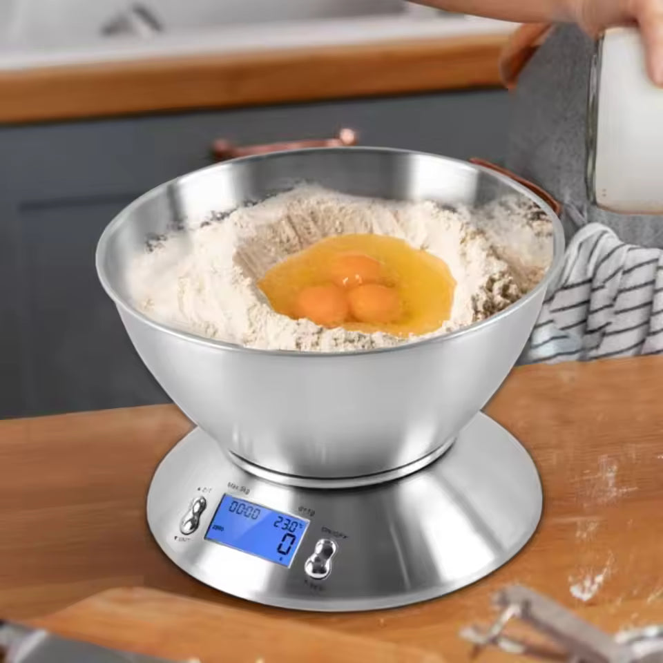 A stainless steel digital kitchen scale with a blue display sits on a wooden countertop, measuring flour and three eggs in a large metal mixing bowl. A person's hand and arm are visible at the top holding a glass of milk, in a kitchen setting.