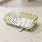 A translucent sage green plastic dish rack with a white slotted tray, a white cup holder, and gold-toned hardware, shown on a light beige stone surface.