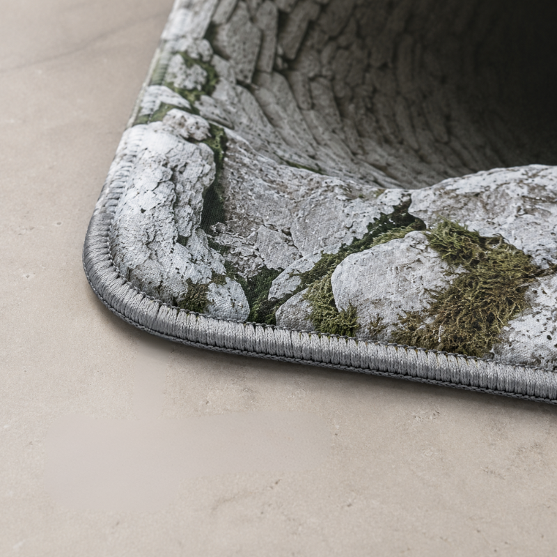 Close-up of a textured rug corner with a bark and moss pattern in gray, white, and green, shown on a beige floor.