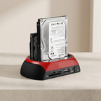 A red and black external hard drive dock with two hard drives inserted, shown on a beige tabletop against a neutral beige background.