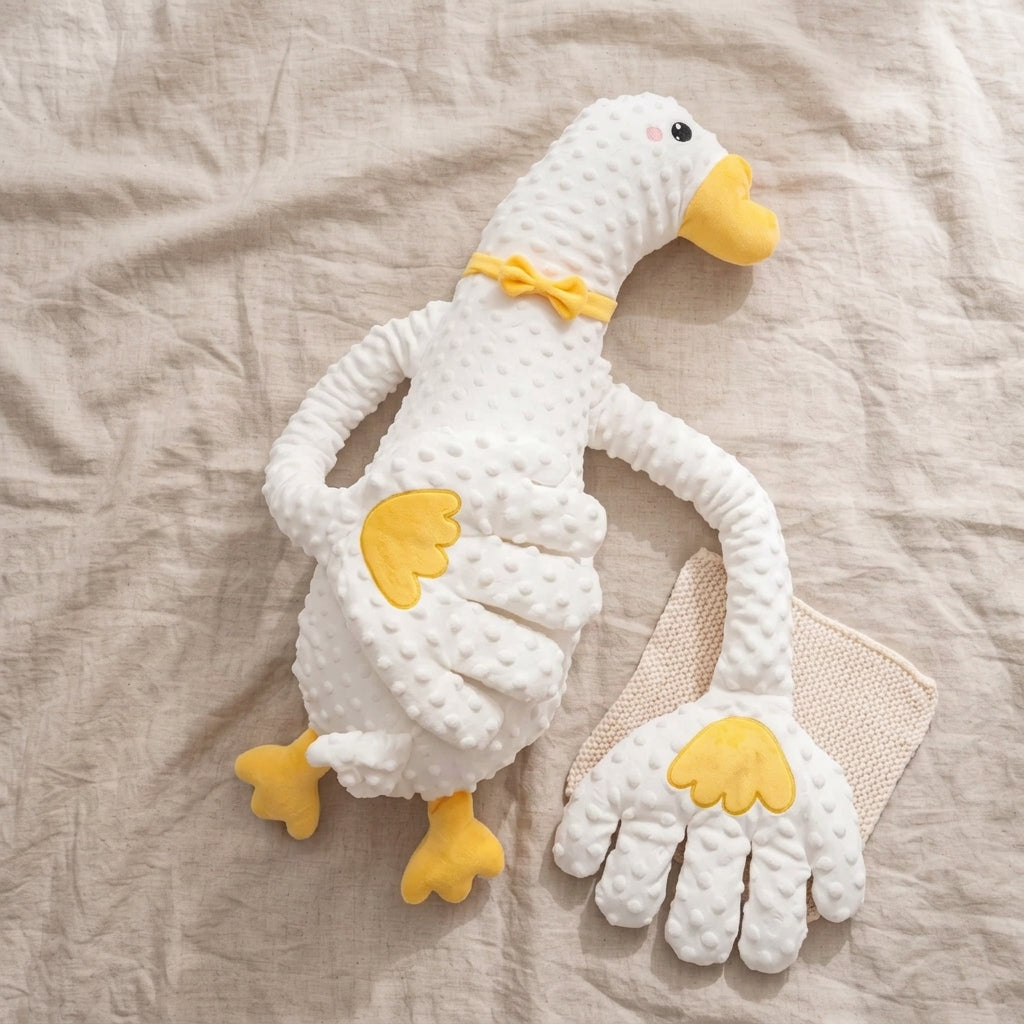 A white textured plush goose toy with yellow beak, feet, and wing details, posed on a beige linen fabric background next to a matching beige cloth.