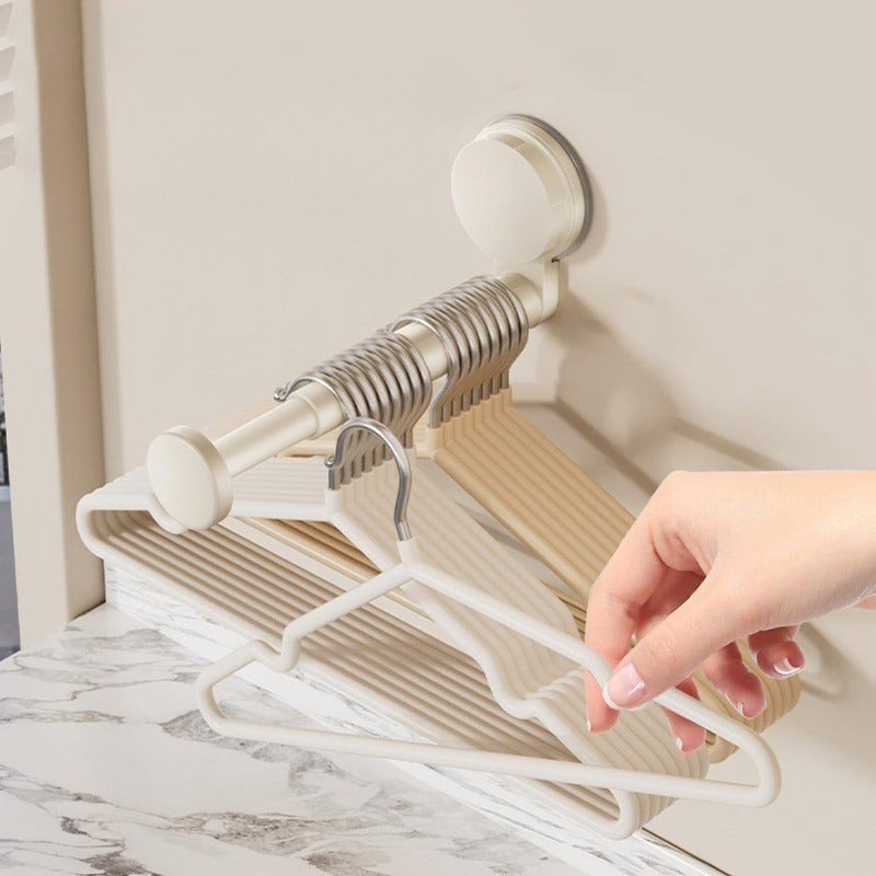 A wall-mounted hanger rack with a suction cup, holding multiple beige and white hangers, shown with a hand adjusting them against a light beige wall above a marble surface.