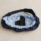 A padded waist bag or fanny pack in navy blue fabric with a light blue patterned inner lining featuring white nautical motifs. The bag has a black plastic buckle and a black fabric loop on the front, photographed on a neutral beige background.