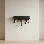 A black wall-mounted shelf with a dripping, melted design, shown against a minimalist beige wall and light wood floor.