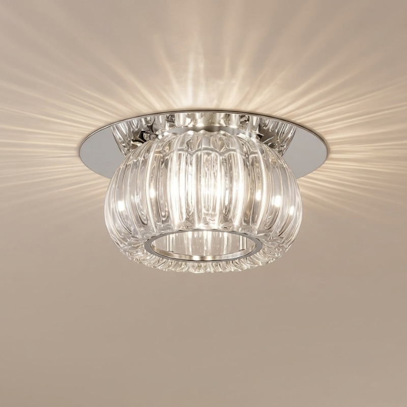 A modern semi-flush mount ceiling light fixture with a clear ribbed glass shade and a polished silver/chrome metal base, shown illuminated against a beige ceiling.
