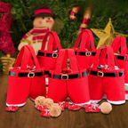 A set of red felt Santa hat-shaped candy baskets with black faux-leather belt details and gold-tone buckle accents, arranged on a wooden surface with wrapped candies and nuts in front. Christmas decorations, including a snowman figure and a star ornament, are blurred in the background.