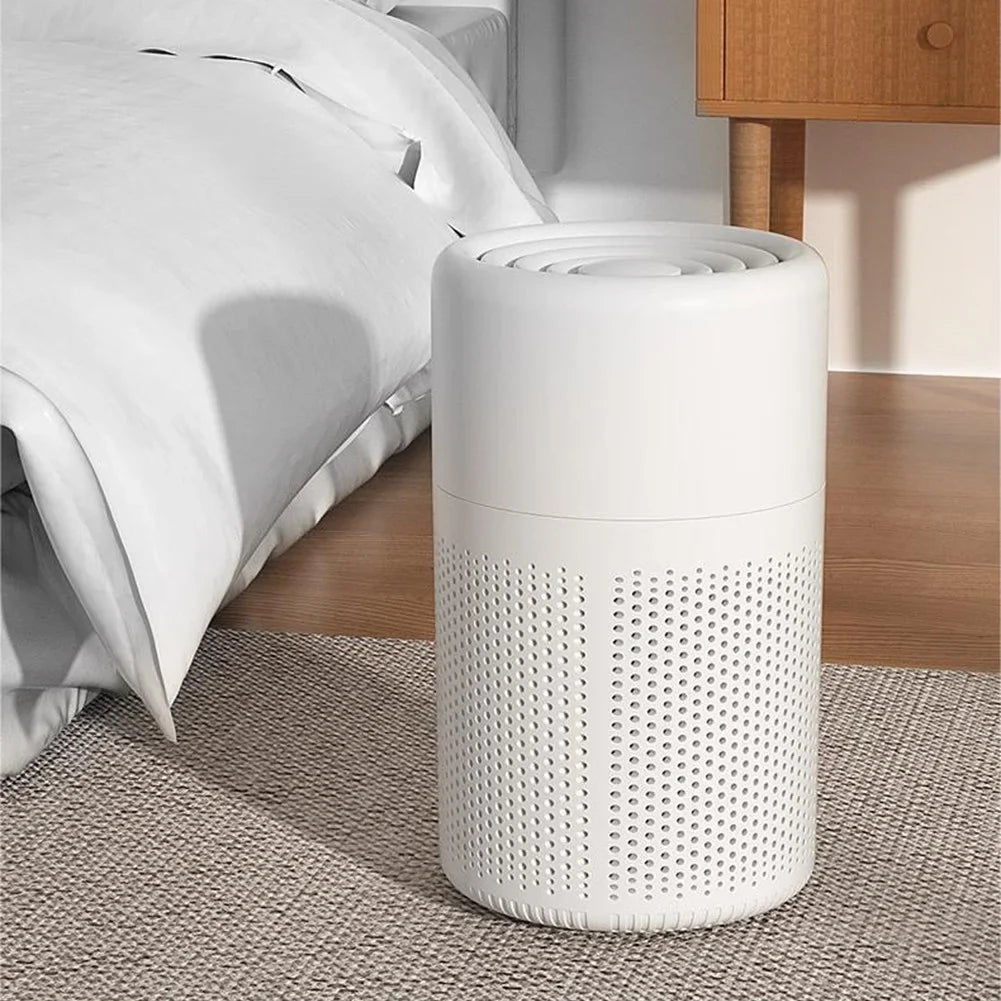 White cylindrical air purifier on a carpeted floor next to a bed