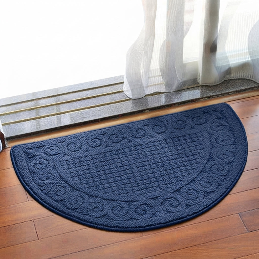 A navy blue semi-circular doormat with a raised textured pattern and decorative border, placed on a wooden floor in front of a glass door with white curtains.