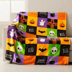 A multicolor Halloween-themed throw blanket draped over a white armchair. The blanket features a patchwork design of orange, purple, green, black, and yellow squares with illustrations of jack-o'-lanterns, ghosts, skulls, bats, cauldrons, and text reading 'Happy Halloween' and 'Trick or Treat'.