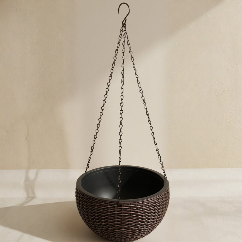 Brown woven hanging planter with chain against a beige wall.