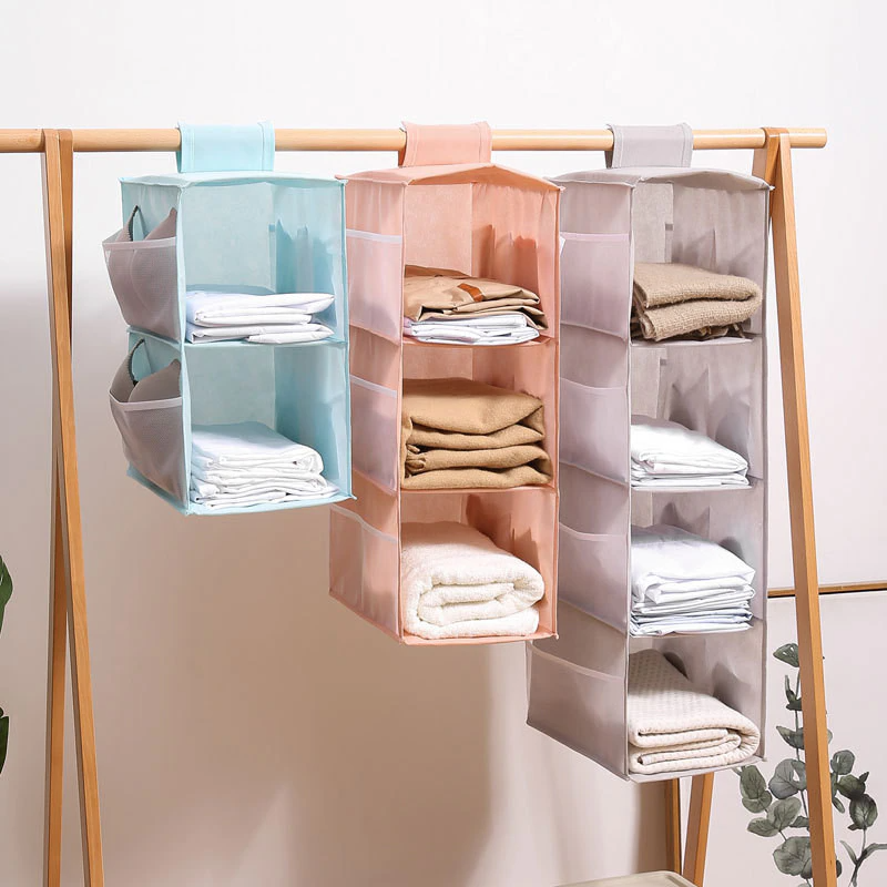Three hanging shelf organizers in different colors with folded clothes on a wooden rack.