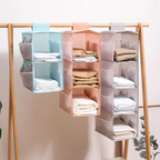Three hanging shelf organizers in different colors with folded clothes on a wooden rack.