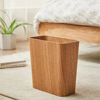 Wooden trash can on a carpeted floor with a bed and plant in the background