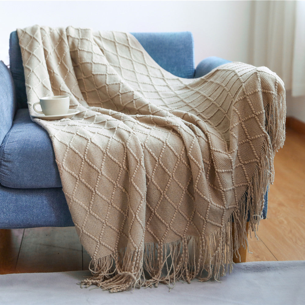 Beige diamond patterned throw blanket draped over a blue sofa with a cup on a wooden table.