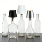 Clear glass bottles with black, white, and silver lampshades on a reflective surface.