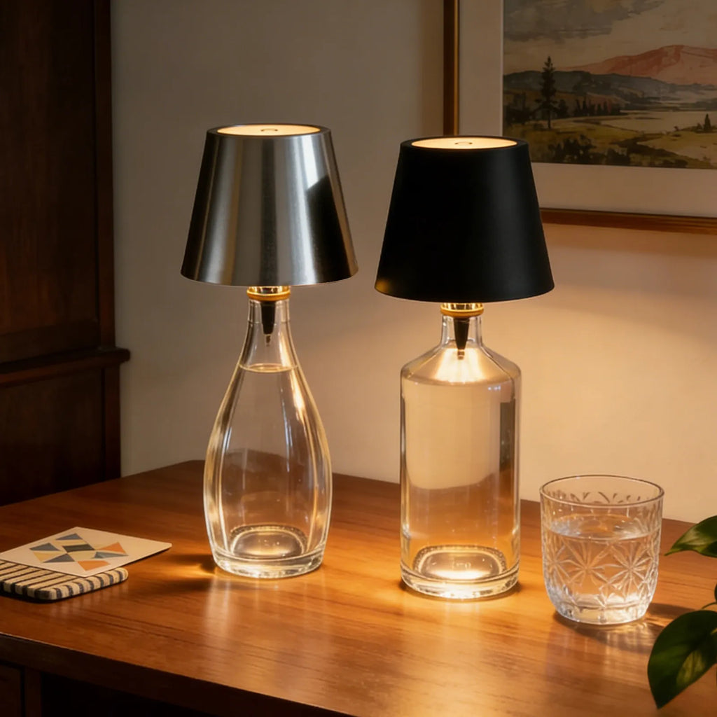 Two glass table lamps with different colored shades on a wooden surface, with a glass of water and a small notebook in the foreground.