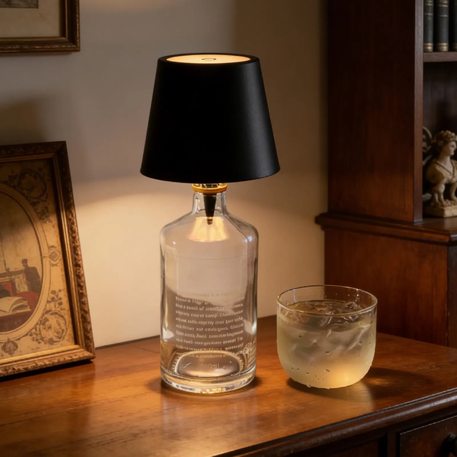 Glass bottle lamp with black shade on a wooden surface next to a glass of water.