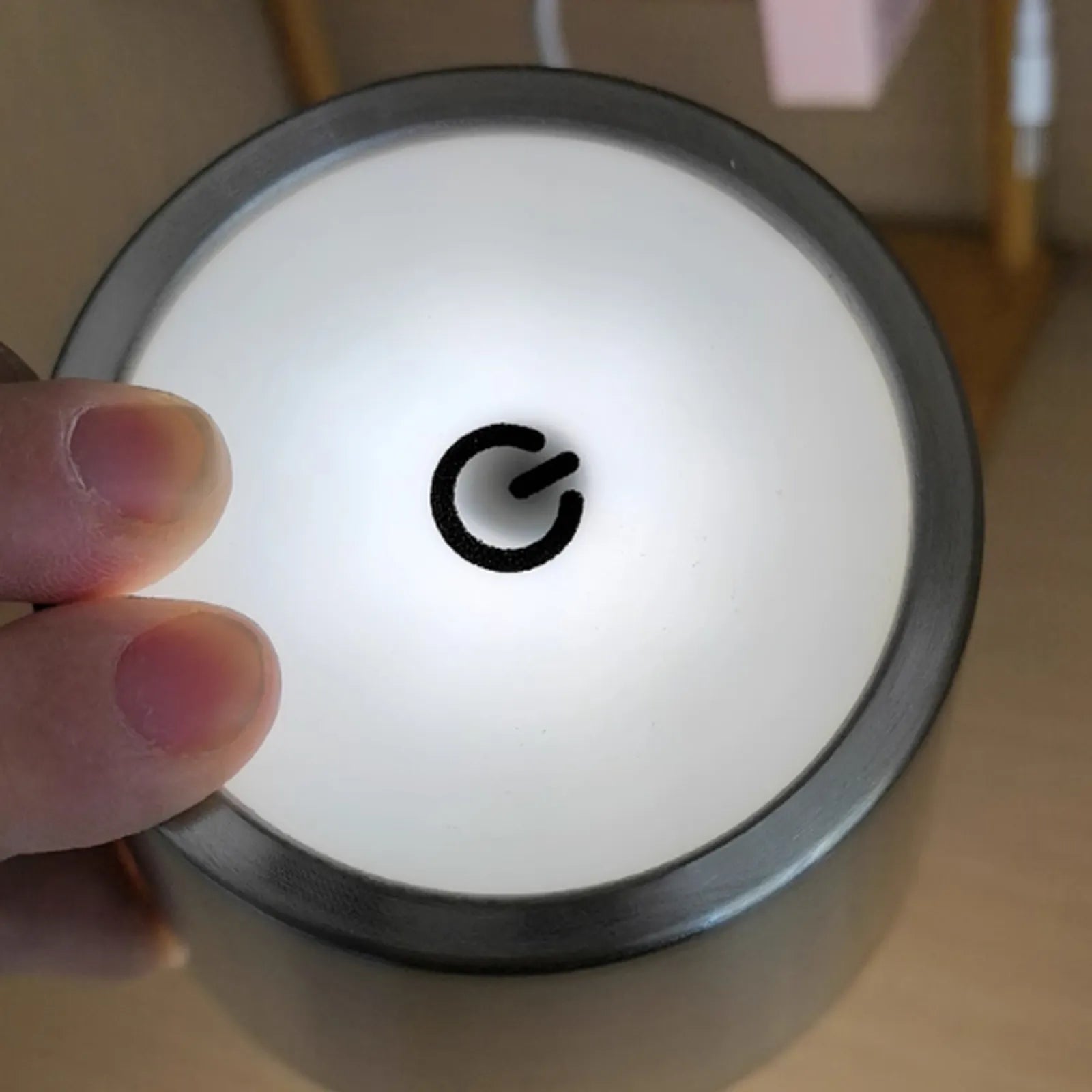 Round device with a power symbol on a white background, held by a hand.