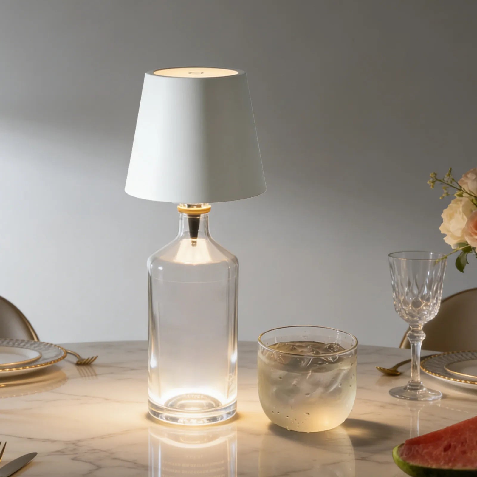 Clear glass table lamp with white shade on a marble surface with dining items.