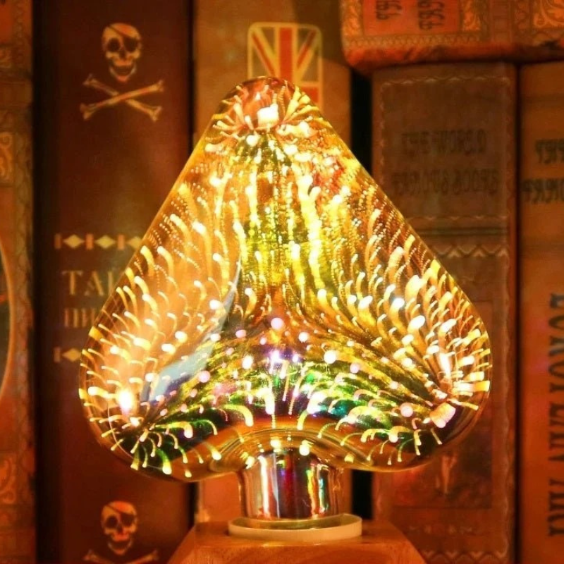 A glowing teardrop-shaped decorative lamp made of textured glass, filled with warm golden light and reflecting multicolored sparkles, set against a background of old book spines.
