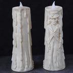Two white wax candles with flame tips, shown against a dark background. One candle has a dripping wax design, and the other features an embossed skeleton figure in formal attire.