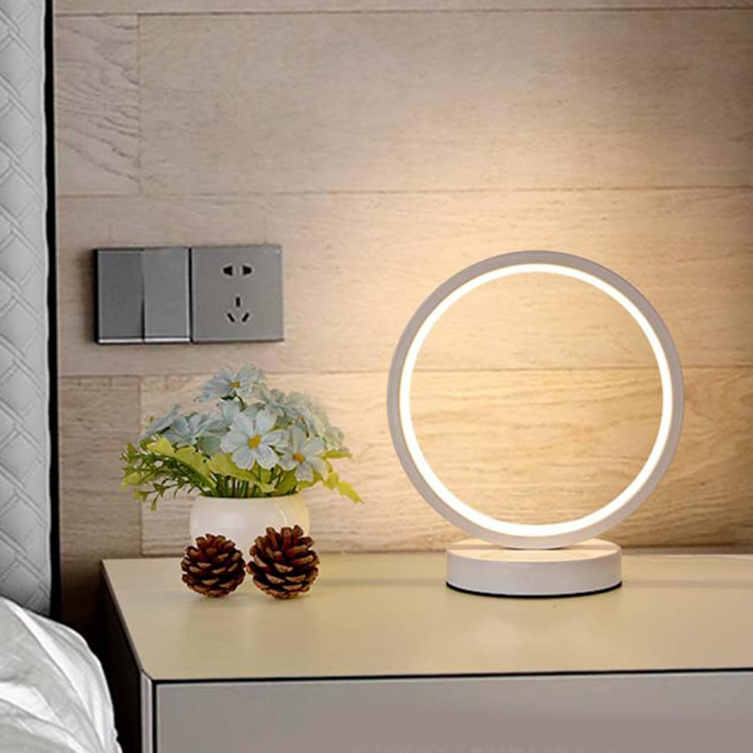Round LED table lamp on a nightstand with decorative items against a wooden wall.