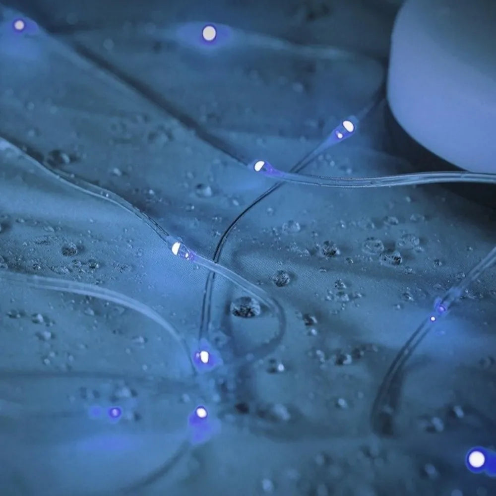 Close-up of clear string fairy lights glowing with blue light, draped over a wet surface with water droplets.