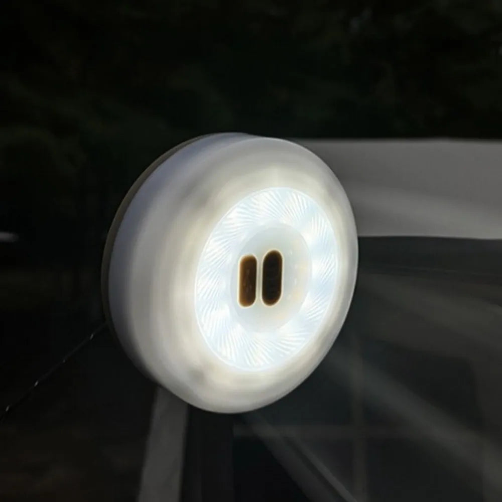 A round white LED window light with a magnetic suction cup base, shown illuminated on a dark glass surface.