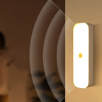 A slim rectangular wall-mounted light fixture with rounded edges, glowing warm white, shown mounted on a beige wall. A small circular yellow detail is visible in the center.