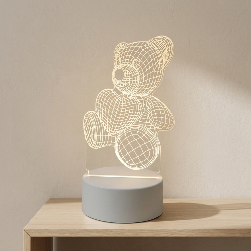 A 3D LED acrylic night light shaped like a teddy bear sitting on a heart, glowing with a warm light. The bear is made of thin white wireframe lines on a clear acrylic panel, mounted on a round matte gray base.