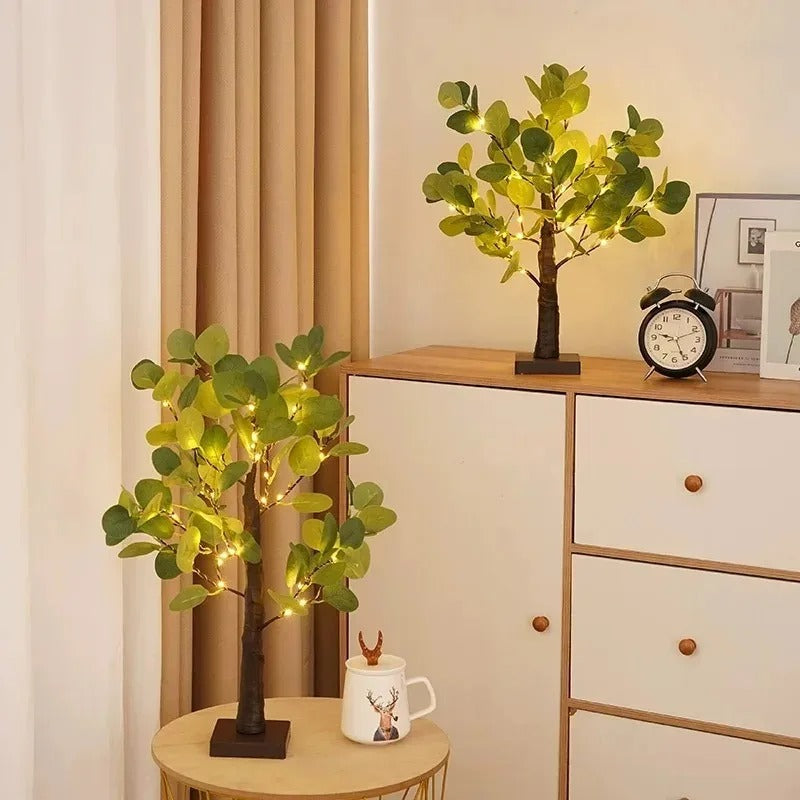 Decorative LED tree lights on a small table with a clock and mug in the background.