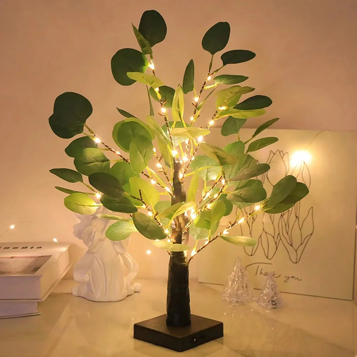 Decorative tree with lights on a table with books and a sculpture in the background