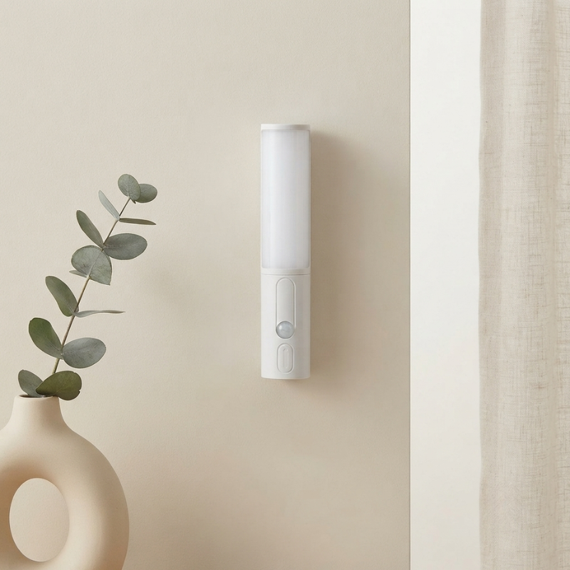 White cylindrical device mounted on a beige wall next to a vase with green leaves.
