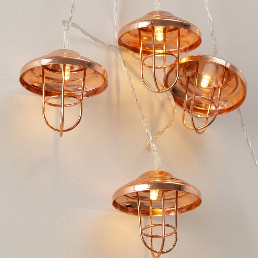 Mushroom-shaped string lights with copper-colored metal caps and wire cages, glowing with warm white bulbs on a light beige wall.
