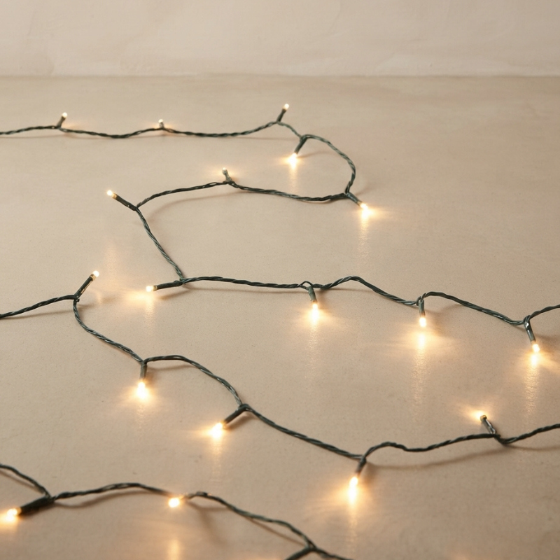 Warm white LED fairy string lights draped across a neutral beige surface, glowing softly with a dark wire.