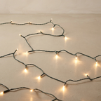 Warm white LED fairy string lights draped across a neutral beige surface, glowing softly with a dark wire.