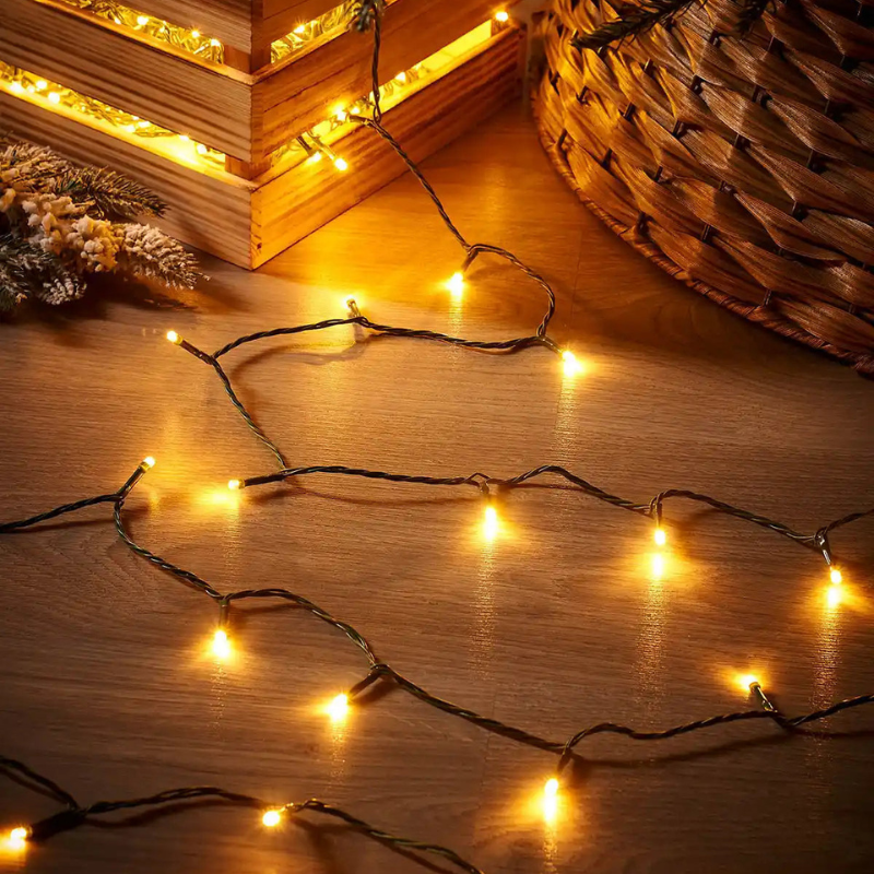 Warm white LED string lights draped across a wooden surface, with a wooden crate and woven basket in the background, creating a cozy holiday atmosphere.