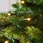 Close-up of green artificial tree branches with warm white string lights glowing softly.
