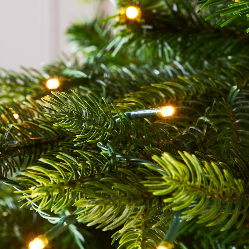 Close-up of green artificial tree branches with warm white string lights glowing softly.